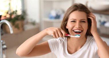 Happy young woman brushing teeth at home