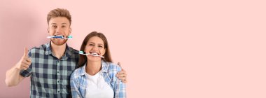 Pembe arka planda diş fırçaları olan komik genç bir çift.