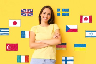 Güzel genç bir kadın ve sarı arka planda farklı bayraklar. Yabancı dil öğrenimi