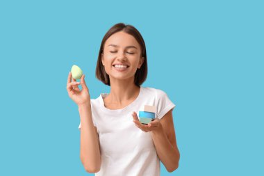 Mavi arka planda makyaj süngeri olan güzel bir genç kadın.