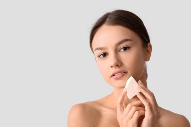 Gri arka planda makyaj süngeri olan güzel bir genç kadın.