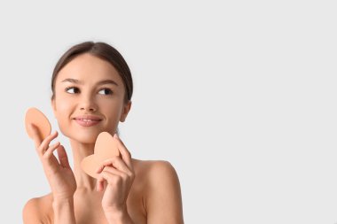 Gri arka planda makyaj süngeri olan güzel bir genç kadın.