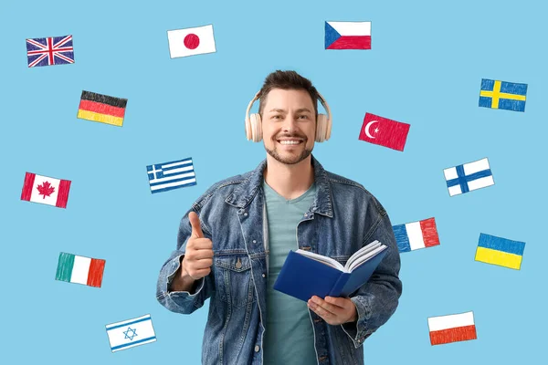 Άντρας Ακουστικά Βιβλίο Και Πολλές Διαφορετικές Σημαίες Γαλάζιο Φόντο Σπουδές — Φωτογραφία Αρχείου