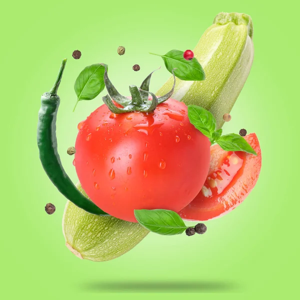 Flying fresh vegetables with spices and basil leaves on green background
