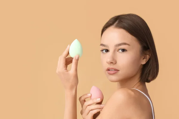 Pretty young woman with makeup sponges on beige background