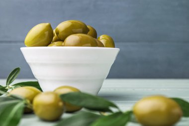 Bowl of green olives on wooden table, closeup
