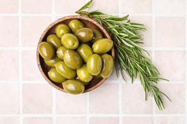 Bowl of green olives and rosemary on color tile