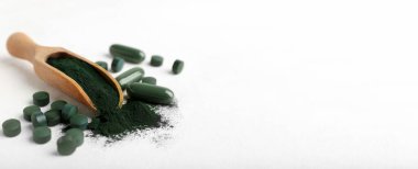 Beyaz arkaplanda bir kepçe spirulina tozu ve haplar.