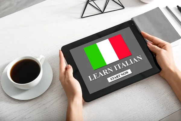 Woman holding tablet computer with text LEARN ITALIAN on screen at workplace
