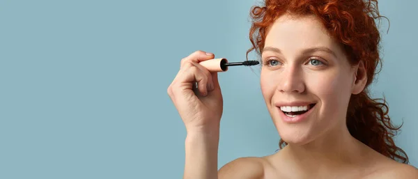 Beautiful Redhead Woman Applying Mascara Blue Background Space Text — Stok Foto
