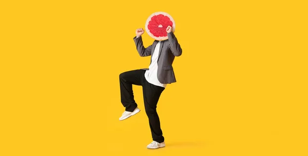 Dancing man with ripe grapefruit instead of his head on yellow background