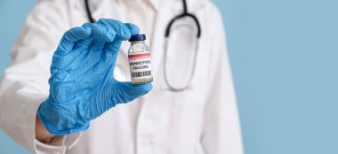 Female doctor with monkeypox vaccine on blue background with space for text, closeup