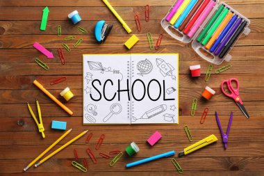Notebook with word SCHOOL and set of supplies on wooden background