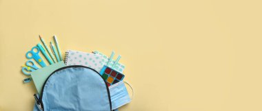 Okul kırtasiyeli sırt çantası ve bej arka planda tıbbi maske ile metin için boşluk