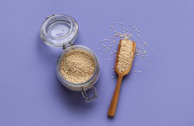 Cam kavanoz ve arkaplanda susam tohumları olan ahşap kepçe