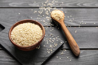 Koyu ahşap arka planda kase ve kaşık dolusu susam tohumu, yakın plan.