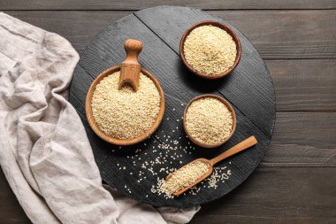 Koyu ahşap arka planda kase ve kepçe susam tohumlarıyla kompozisyon