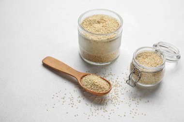 Işık arka planında kase, kavanoz ve kaşık dolusu susam tohumu