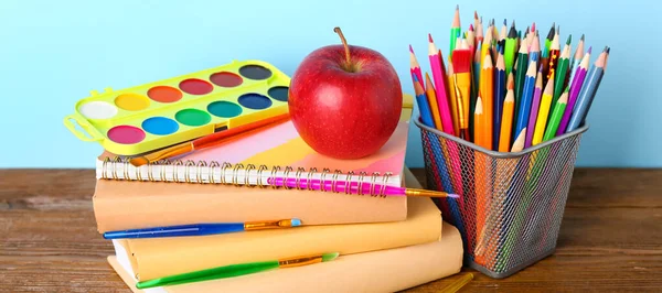 School stationery with apple and paints on table against blue background