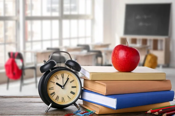 Books with apple and alarm clock on desk in classroom