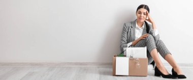 Sad fired woman sitting on floor near light wall