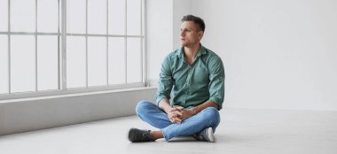 Depresyondaki genç adam boş bir odada yerde oturuyor.