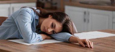 Depressed young woman at table in kitchen