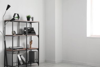 Ofis eşyalarının olduğu raf ve lamba ışıklı duvarın yanında.