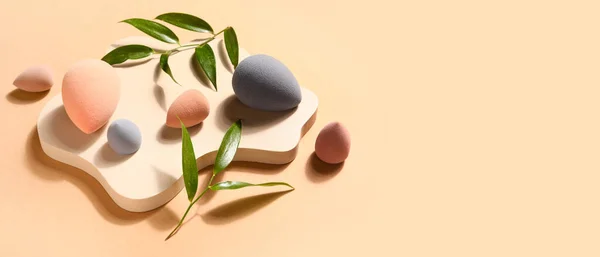 Makeup sponges and plant leaves on beige background with space for text