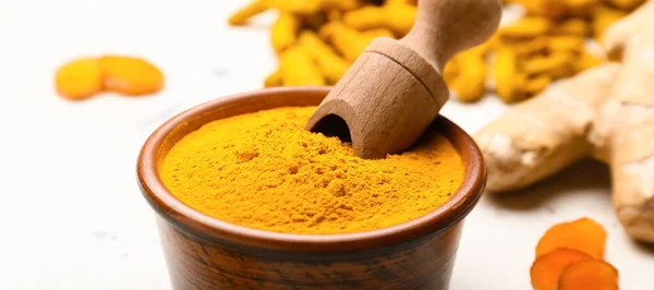 Bowl with aromatic turmeric powder and scoop on table, closeup