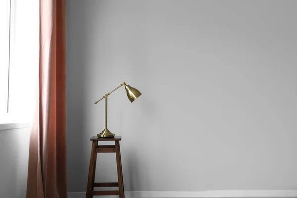 Golden lamp on stool near red curtain in room