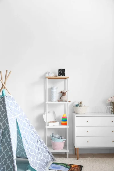 Interior of light children\'s playroom with shelving unit and chest of drawers