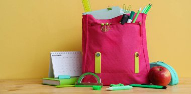 Kırtasiye malzemesi ve elma içeren okul çantası renk arkaplanına karşı 