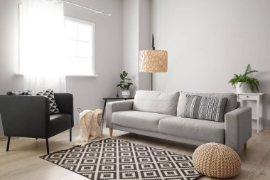 Interior of light living room with grey sofa, tables and armchair