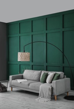 Gri kanepe, ekose sepet, çiçek ve yeşil duvarın yanında standart lamba.