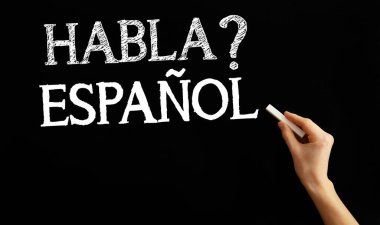 Hand writing text HABLA ESPANOL? (DO YOU SPEAK SPANISH?) on black background