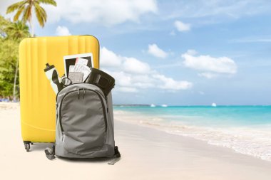 Kumsalda plaj aksesuarlarıyla dolu valiz ve sırt çantası. Seyahat kavramı