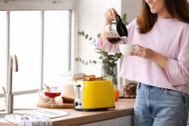 Güzel genç Asyalı kadın kahve içiyor ve mutfakta lezzetli tost yapıyor.