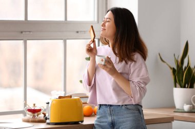 Güzel genç Asyalı kadın kahve içiyor ve mutfakta lezzetli tost yapıyor.