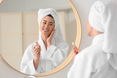 Genç Asyalı kadın banyoda kozmetik serumu kullanıyor.