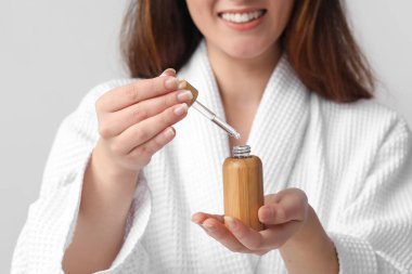 Gri arka planda kozmetik serumu olan genç bir kadın. Yakın plan.