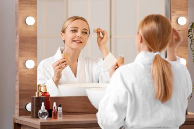 Banyoda kozmetik serumu kullanan olgun bir kadın.