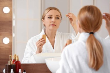 Banyoda kozmetik serumu kullanan olgun bir kadın.