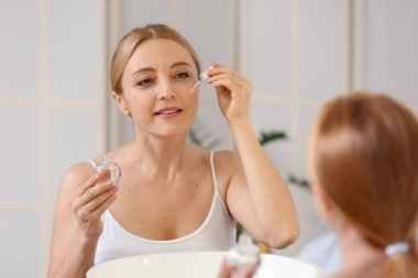 Banyoda kozmetik serumu kullanan olgun bir kadın.