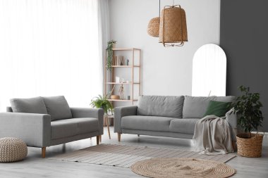 Gri koltukları, raf ünitesi ve ev bitkileriyle aydınlık oturma odasının içinde.