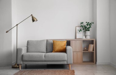 Interior of light living room with grey sofa, lamp and shelving unit