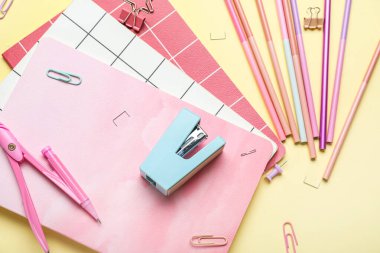 Stapler with different stationery supplies on yellow background