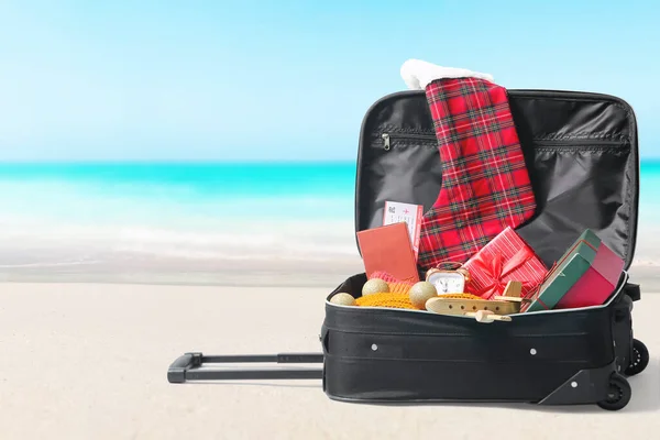 Open suitcase with beach accessories on sand at resort. Christmas vacation