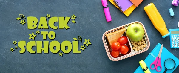 Lunch box with tasty food and school stationery on dark background