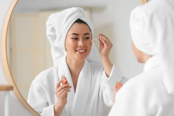 Young Asian woman using cosmetic serum in bathroom